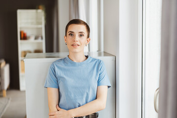 Confident Young Woman in Blue T-Shirt Invitingly Gazes into the Camera in Modern Living Room