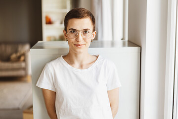 Confident Young Woman with Short Hair, Glasses, and T-Shirt, Gazing Intently in Contemporary Living...