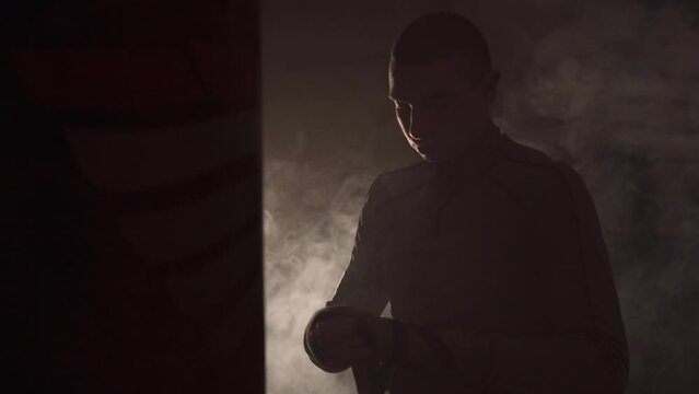 Closeup of man wrapping sport protective bandages on his hands on dark smoke background, preparing for tough fight