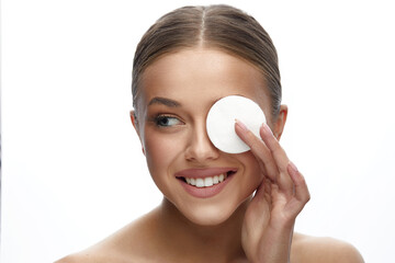 Close up beauty portrait of a young attractive woman cleaning her face with a cotton pad isolated over white background