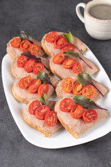 Homemade sandwiches with turkey pate and cherry tomatoes, also a cup of coffee on gray background
