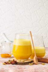 Turmeric latte or golden milk drink in glass with ingredients for its preparation spices, cardamom, cinnamon stiks with copy space for recipe