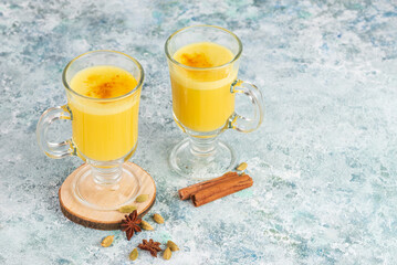 Two servings of turmeric latte or golden milk with spices cardamom, cinnamon stiks, anis stars  on the blue background with copy space