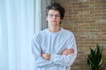 Portrait of handsome guy 18, 19 years old with crossed arms in home interior