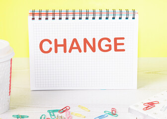 CHANGE the word is written on a blank sheet in a notebook standing on a table on a yellow background