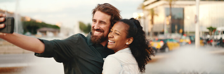 Closeup of smiling interracial couple taking a selfie on fountain background. Close-up, man and woman video chatting using a mobile phone - Powered by Adobe