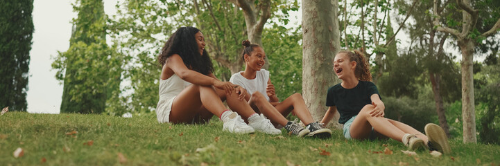 Three girls friends pre-teenage sit on the grass in the park and emotionally talking. Three...