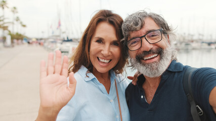 Close-up of smiling elderly couple taking selfie while standing in marina on yacht background