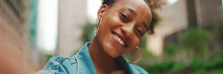 Fotobehang Closeup portret cute African girl with ponytail, wearing denim jacket makes stream, video call on smartphone in modern city background. © Andrii Nekrasov