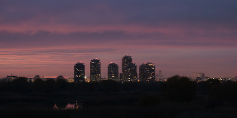 Bucharest night city skyline panorama in Romania capital, with tall buildings and pink, purple twilight colors.