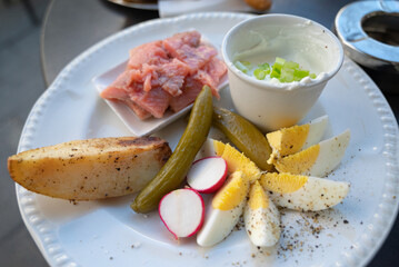 A plate of delicacies: pickled herring fish, baked potato, slices of hard-boiled egg, pickled cucumber and radish