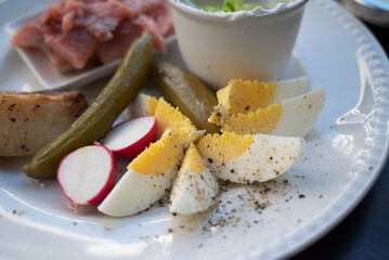 A plate of delicacies: pickled herring fish, baked potato, slices of hard-boiled egg, pickled cucumber and radish