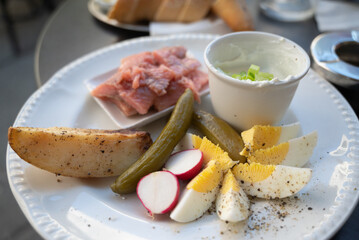 A plate of delicacies: pickled herring fish, baked potato, slices of hard-boiled egg, pickled cucumber and radish