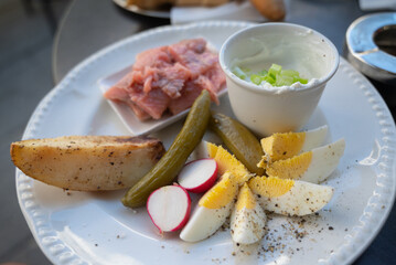 A plate of delicacies: pickled herring fish, baked potato, slices of hard-boiled egg, pickled cucumber and radish