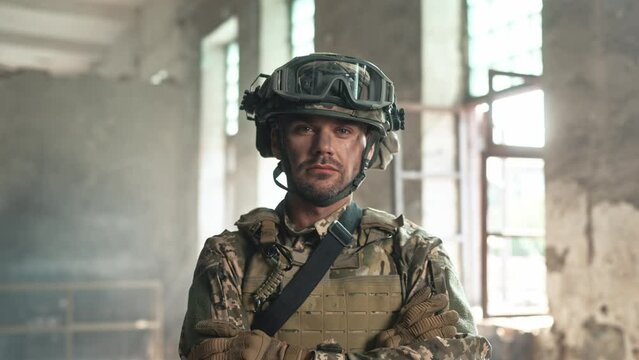 Handsome soldier in military uniform wearing helmet and bulletproof vest standing in abandoned buildings. Strong warrior seriously looking at camera. Protecting country from aggressor.