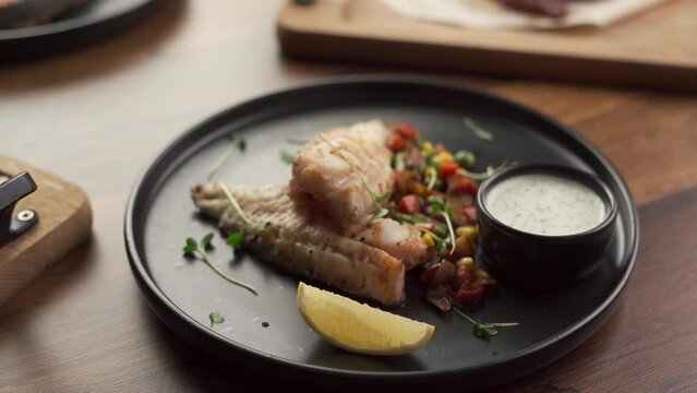 Grilled fish fillet with BBQ vegetables served on black plate in the restaurant. Seafood dinner concept