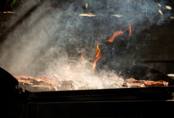 Barbacoa con llamas y humo cocinando carne a la brasa - obrazy, fototapety, plakaty