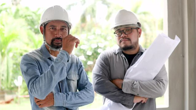 Two partner contractors, foreman, manager male arm crossed looking at camera, young architect employee holding blueprint paperwork with middle-aged Indian project builder, team labor worker inspection