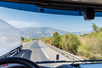 View from the driver's seat of a truck of another refrigerated truck overtaking on a highway. - obrazy, fototapety, plakaty