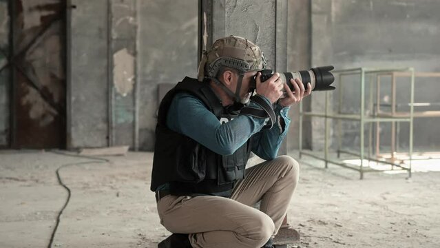 Military photojournalist in protective equipment taking photo with camera in abandoned building. Caucasian man photographing ruins in war zone. Dangerous work. Mass media during military conflict.
