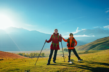 Young woman tourist with son standing in green mountain valley at sunny day