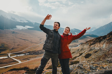 Happy tourist couple waving hands in mountain valley in autumn