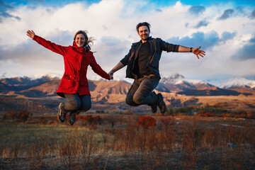 Happy tourist couple jumping on mountains background in autumn