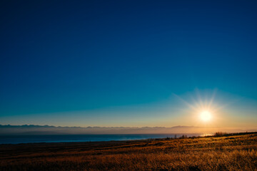 Picturesque rural landscape with field and lake at sunset