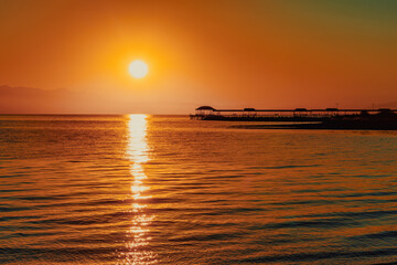Fiery red sunset over lake with pier silhouette