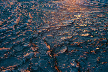 Surface of cracked ice on lake at sunset light