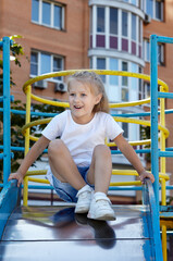 Little girl playing on a slide in a playground in the summer city park. Childhood, leisure and...