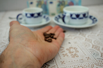 hand with grains of coffee and two cups of coffee