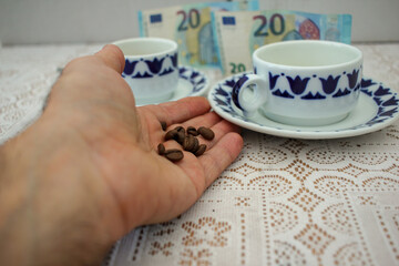 hand with grains of coffee, cups of coffee and euro bills