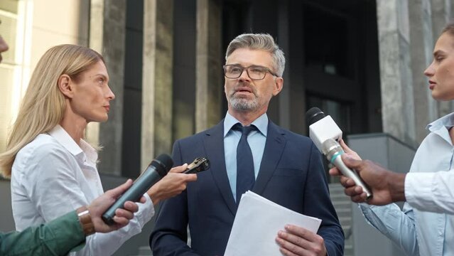 Group of mixes-raced journalists standing around successful political man in middle of street. Hardworking reporters asking questions during press conference. Big event on television.