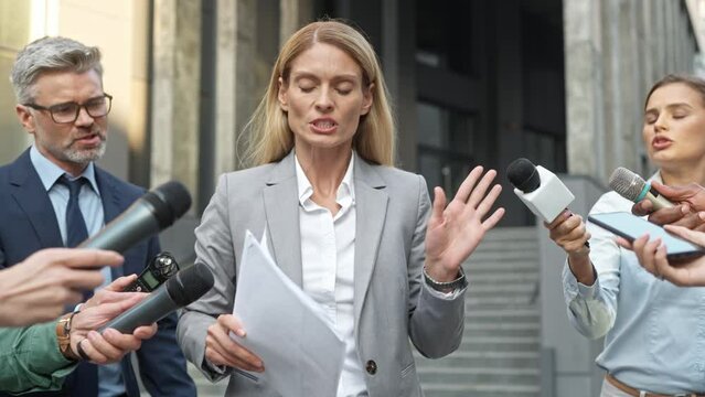 Inquisitive journalists trying to get interview by political woman. Upset business lady with documents in her hands walking past reporters and avoiding communication. Inconclusive press conference.