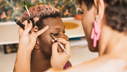 African transgender man with his eyes closed as a colleague applies make-up