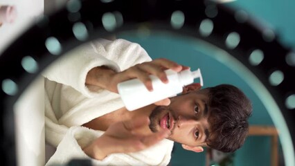Young influencer applying hand cream and vlogging through mobile phone at home