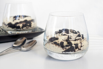 cookie and cream cheesecake in a short glass with spoon on white table.