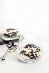 cookie and cream cheesecake in a short glass with spoon on white table.