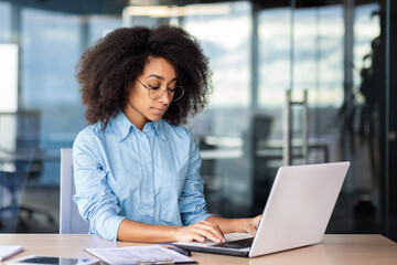 Serious thinking focused woman at workplace inside office working with laptop, business woman typing on keyboard.