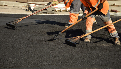 workers with rakes level the asphalt mixture - obrazy, fototapety, plakaty