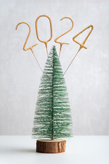 Miniature artificial Christmas tree and golden number 2024 on wooden stand on white background. Vertical frame