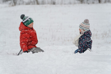 Fototapeta na wymiar Two children sit in the snow on frosty day. Winter holidays. Siblings are played outside in the winter.