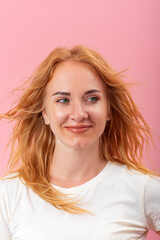 Portrait of young round-faced woman with blond hair. Girl on pink background looks to the side.