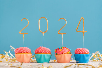 Holiday muffins with pink butter cream and 2024 numbers on blue background. Happy New Year theme.