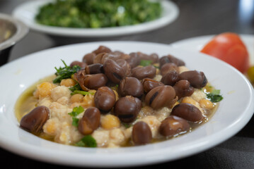 Hummus, a traditional Middle eastern Arabic style mashed chickpeas dish, with baked beans of Vicia Faba, served in a white bowl with olive oil