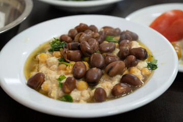 Hummus, a traditional Middle eastern Arabic style mashed chickpeas dish, with baked beans of Vicia Faba, served in a white bowl with olive oil
