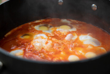 Shakshouka, a traditional dish of poached eggs in a sauce of tomatoes, harissa, olive oil, red peppers, onion and garlic, spiced with cumin, paprika and cayenne pepper