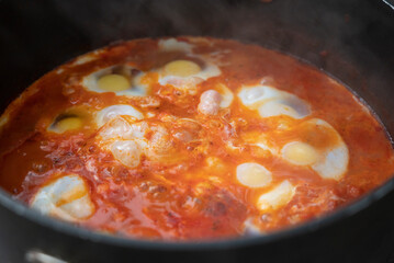 Shakshouka, a traditional dish of poached eggs in a sauce of tomatoes, harissa, olive oil, red peppers, onion and garlic, spiced with cumin, paprika and cayenne pepper
