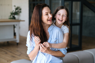 Headshot of young woman embracing daughter, having fun together